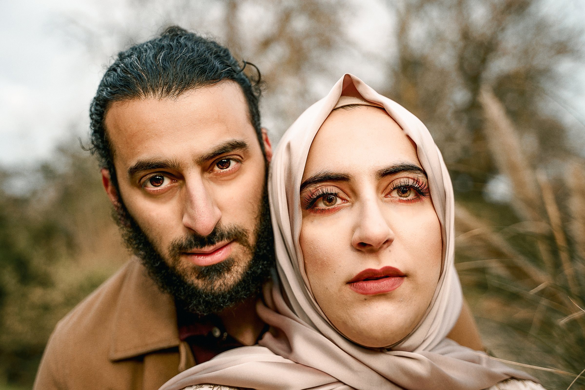 An expectant couple standing together beneath the trees