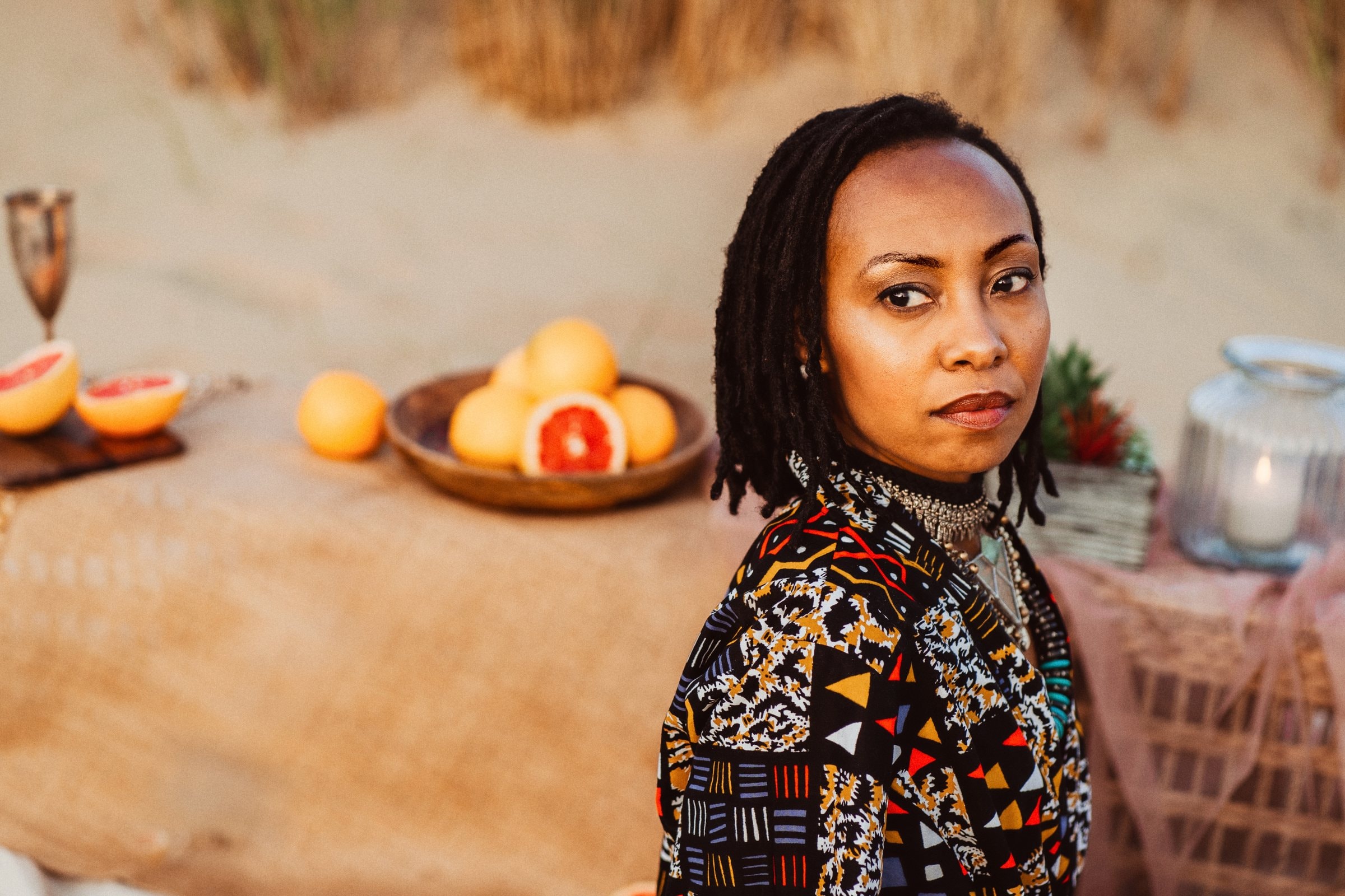 Darla seated beside fruit and textiles at the beach