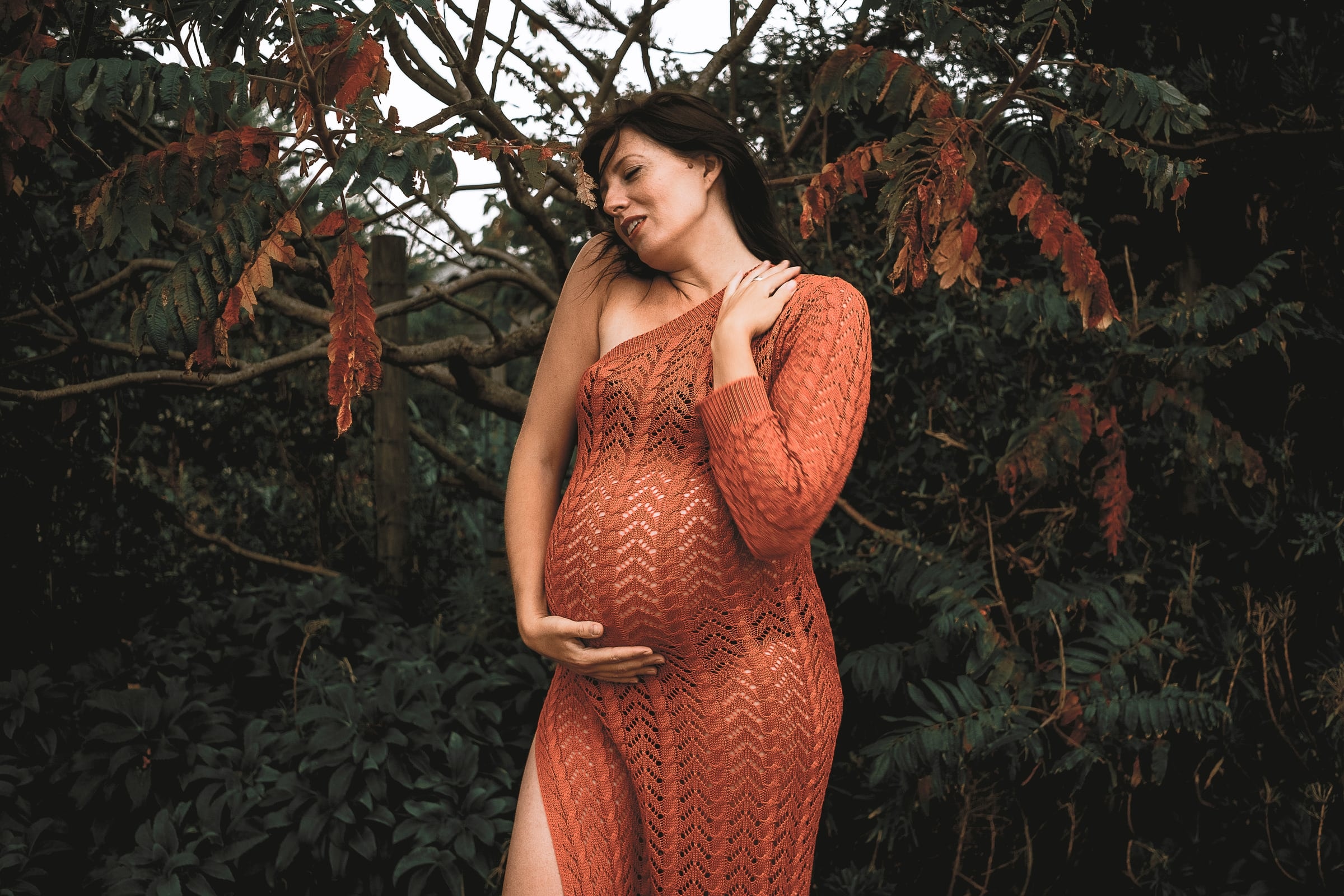 Pregnant woman in rust knitwear in a woodland garden